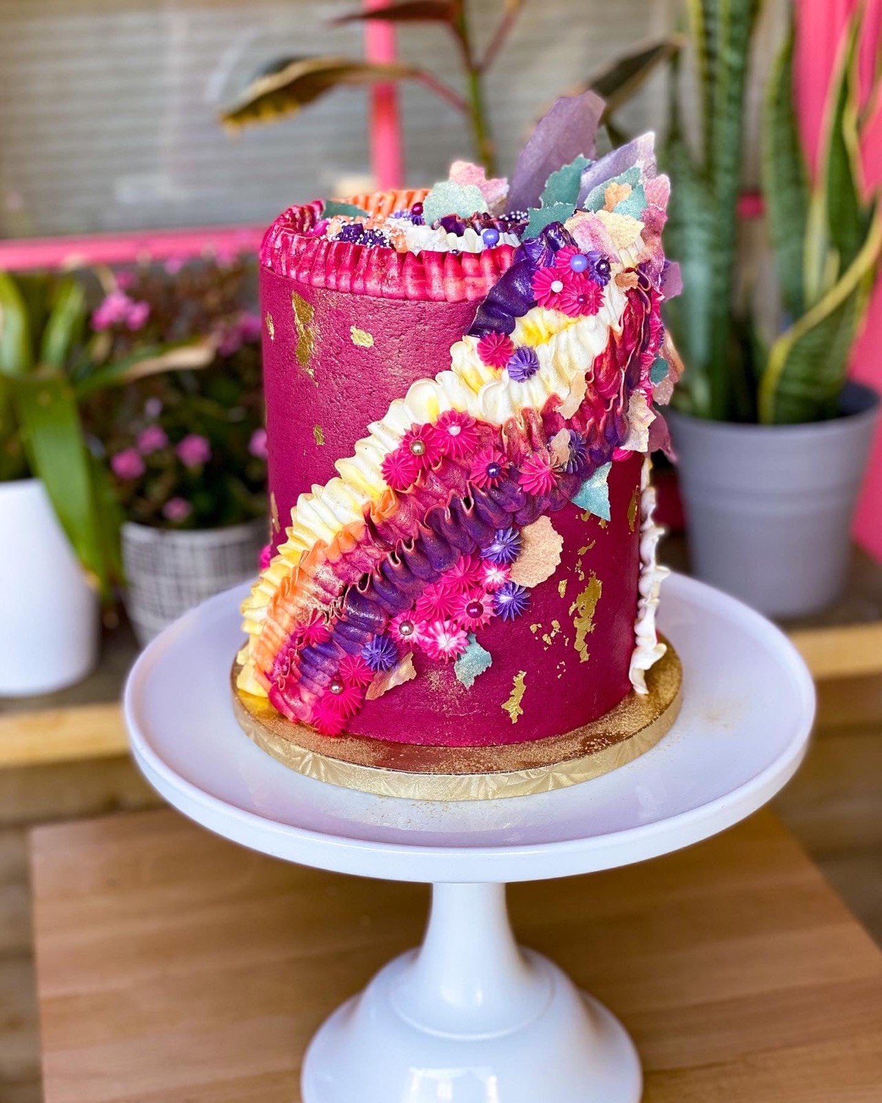 Magenta six-layer celebration cake with edible flowers and gold leaf on a cake stand